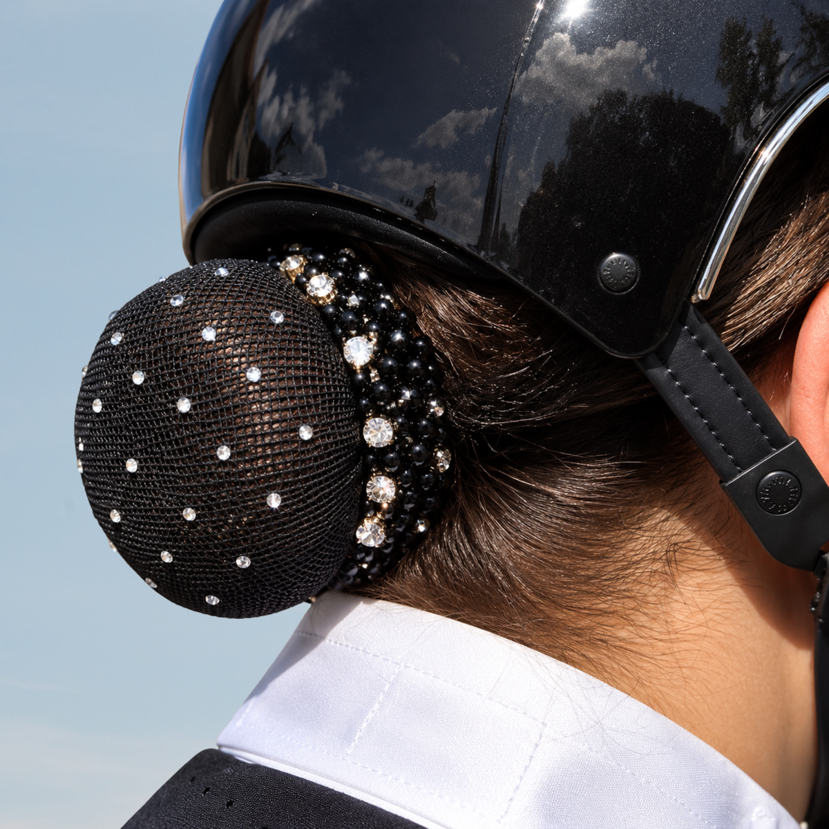 A close-up of a person wearing a black equestrian helmet and white collared shirt, showing a black mesh hair net decorated with rhinestones on the back of the head.