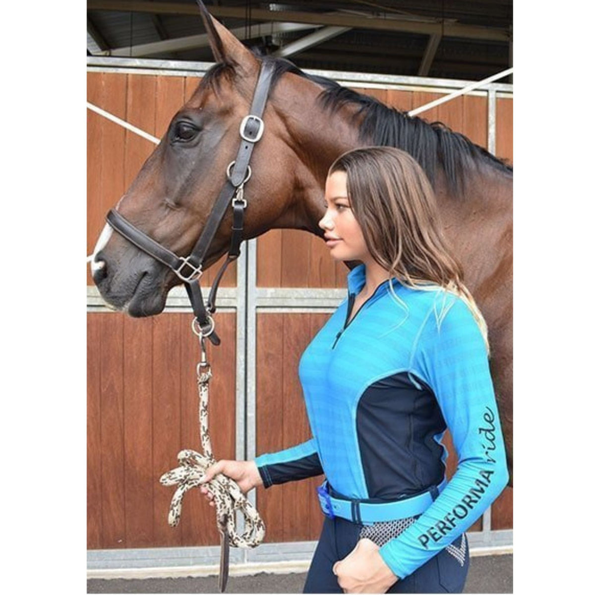 Lady wearing aqua long sleeve riding shirt with navy sides, holding horse.
