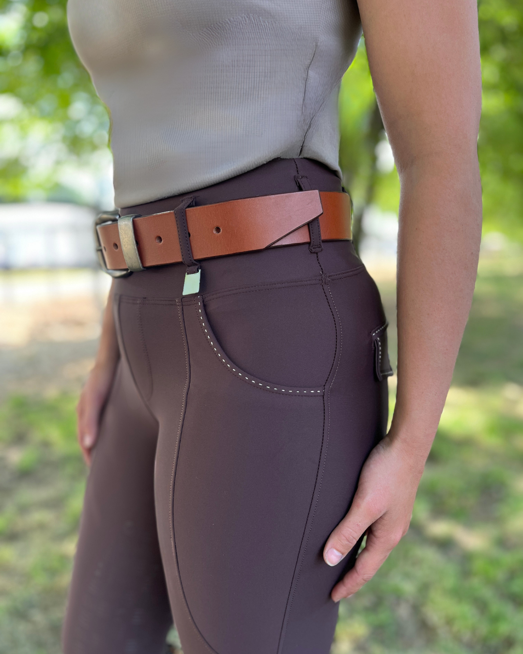 Person wearing brown riding pants with a patterned design, standing outdoors.